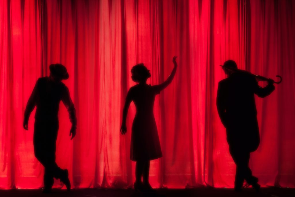 Vor einem roten Vorhang beginnen Silhouetten zu tanzen.
